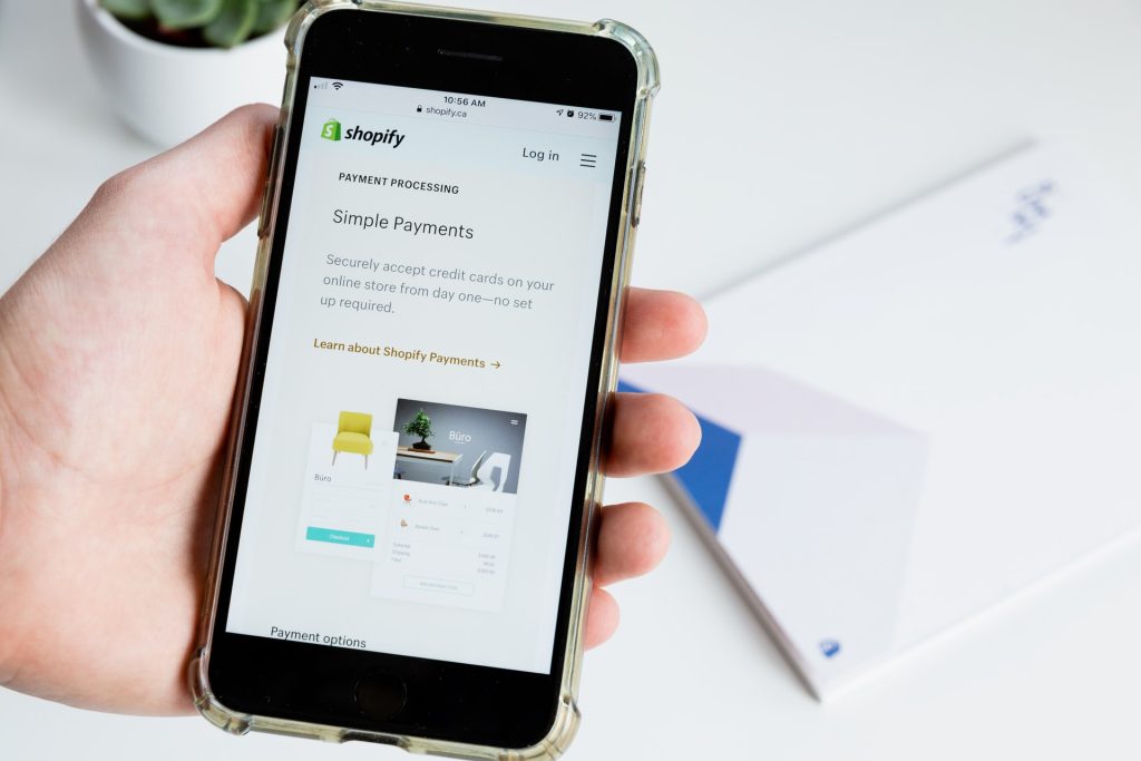 A hand holds a phone with Shopify's website pulled up on it