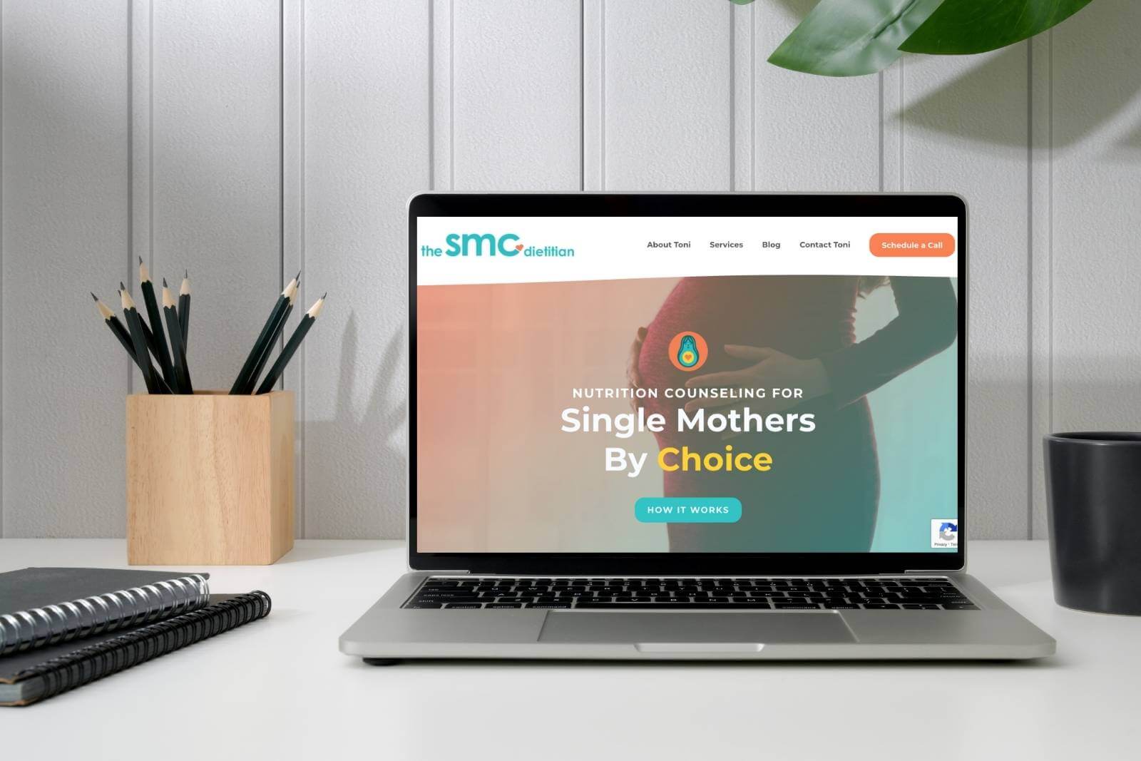 A mockup of The SMC Dietitian's website on a Mac laptop with a pencil holder on the left and a plant on the right
