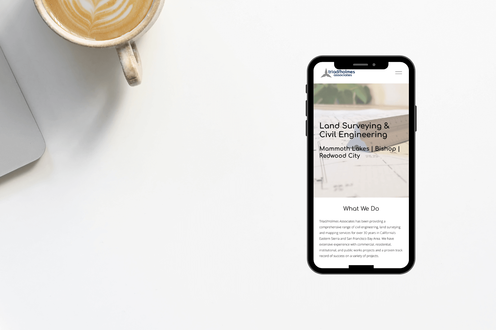 A mockup of Triad/Holmes Associates' website on a cell phone with a latte in the background