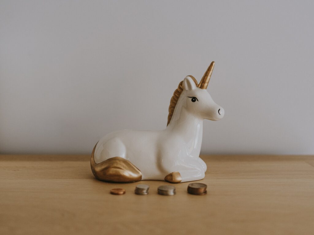 A white unicorn with gold mane and tail and horn sits behind four small piles of coins